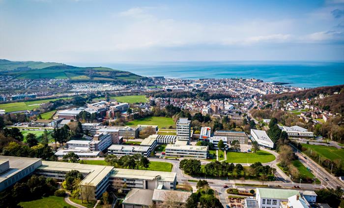 An aeriel view of Aberystwyth University, looking out towards Aberystwyth town and the sea beyond on a bright sunny day